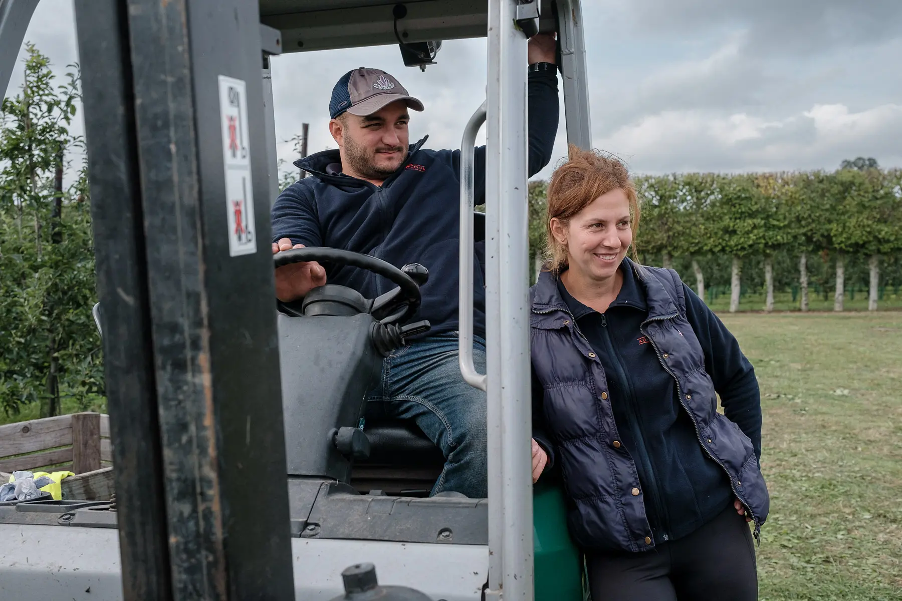 Tractor driver sits in a small tractor and the farm supervisor stands next to the tractor.