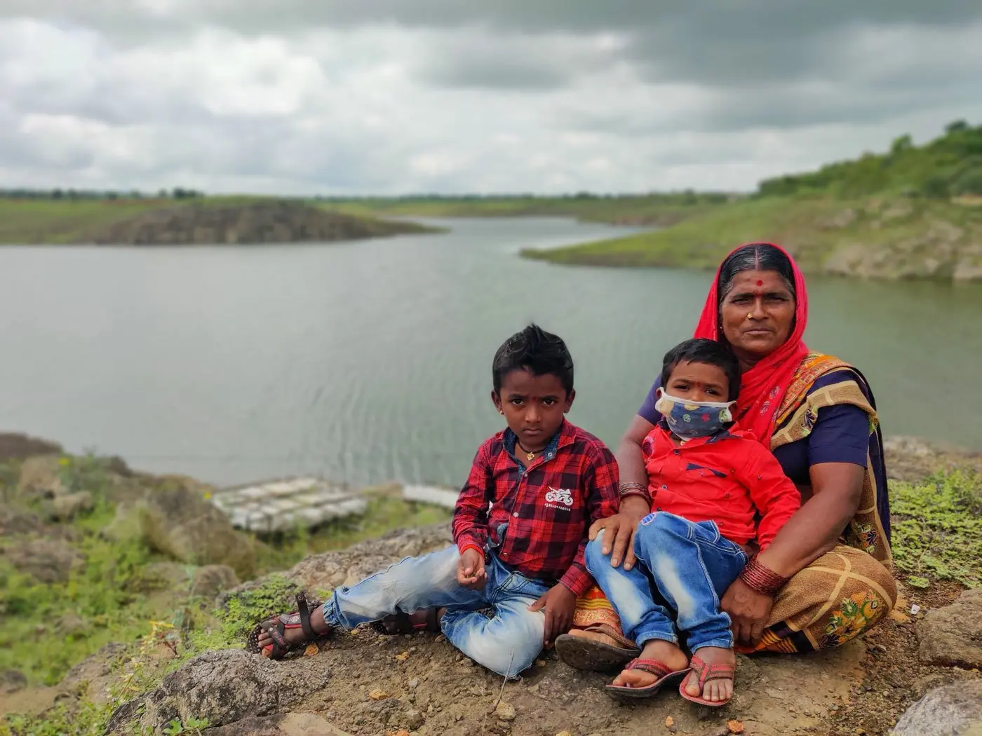 Grandmother sits along a river bank with two children