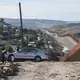 Men gather to fix a car in the Libertad Parte Alta neighborhood of Tijuana, Mexico, left, as the border wall stretches on for miles nearby. Image by Amanda Cowan. Mexico, 2019.