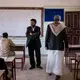 Hussein al Tawushi (center left), principal at the school where Yahya (center right) teaches, looks over students as they take their final exams. Image by Alex Potter. Yemen, 2018.