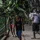 Remy Fernandez, carrying grandchild RJ, makes way for a porter carrying lotus leaves to market. She must make an hour-long climb up a mountain trail to where she can buy produce directly from farmers to sell at a higher rate of profit. Image by James Whitlow Delano. Philippines, 2018.