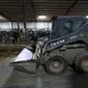 A worker drives a skid loader in one of three barns at Drake Dairy Inc. Image by Mark Hoffman. United States, 2019.