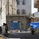 Children gather around their father as he fixes a solar panel for electricity. A blue tarpaulin in the background blocks the line of sight of pro-Houthi snipers in the no-mans-land between the warring factions who have been battling for control of the city of Taiz since May 2015. Image by Iona Craig. Yemen, 2017.