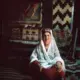 Zina Parvwen, 52, sits before a display of the Wakhi traditional carpets that she and eleven other women make and sell in Gulmit. Image by Sara Hylton/National Geographic. Pakistan, 2019.